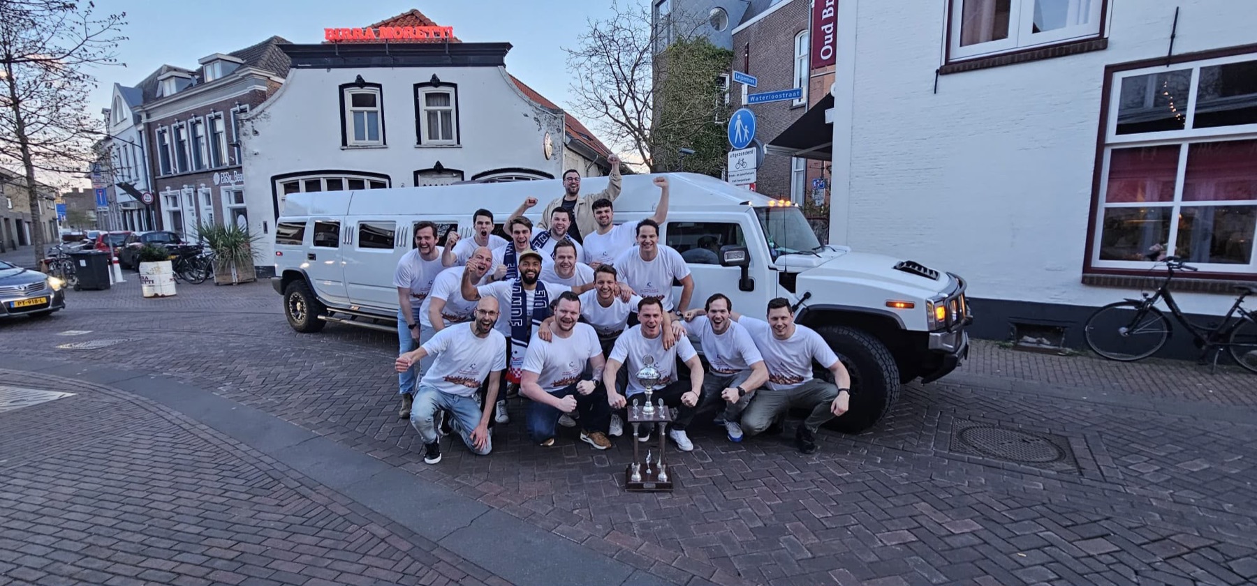 Heren 1 in feestshirts met de beker voor een witte limousine